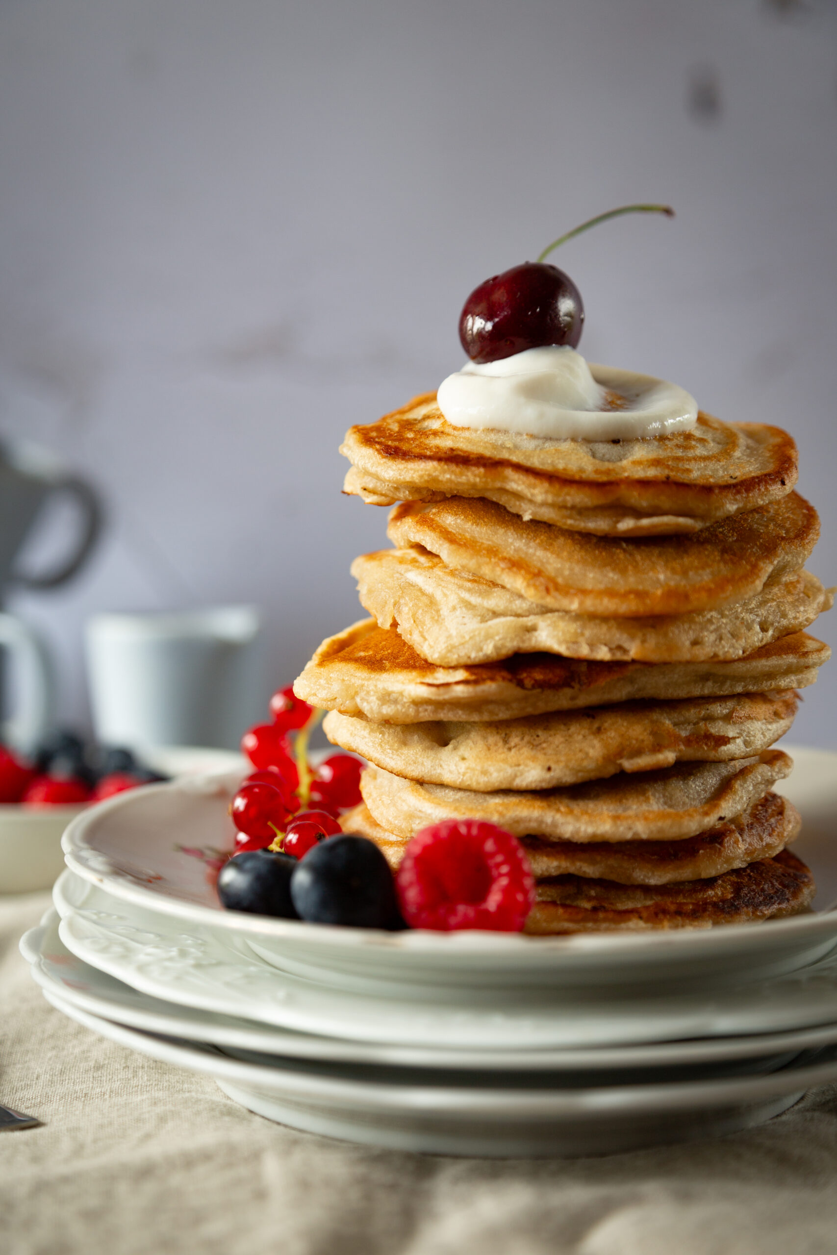 Aufgestapelte fluffige Pancakes, serviert mit Joghurt und frischen rötlichen Beeren.