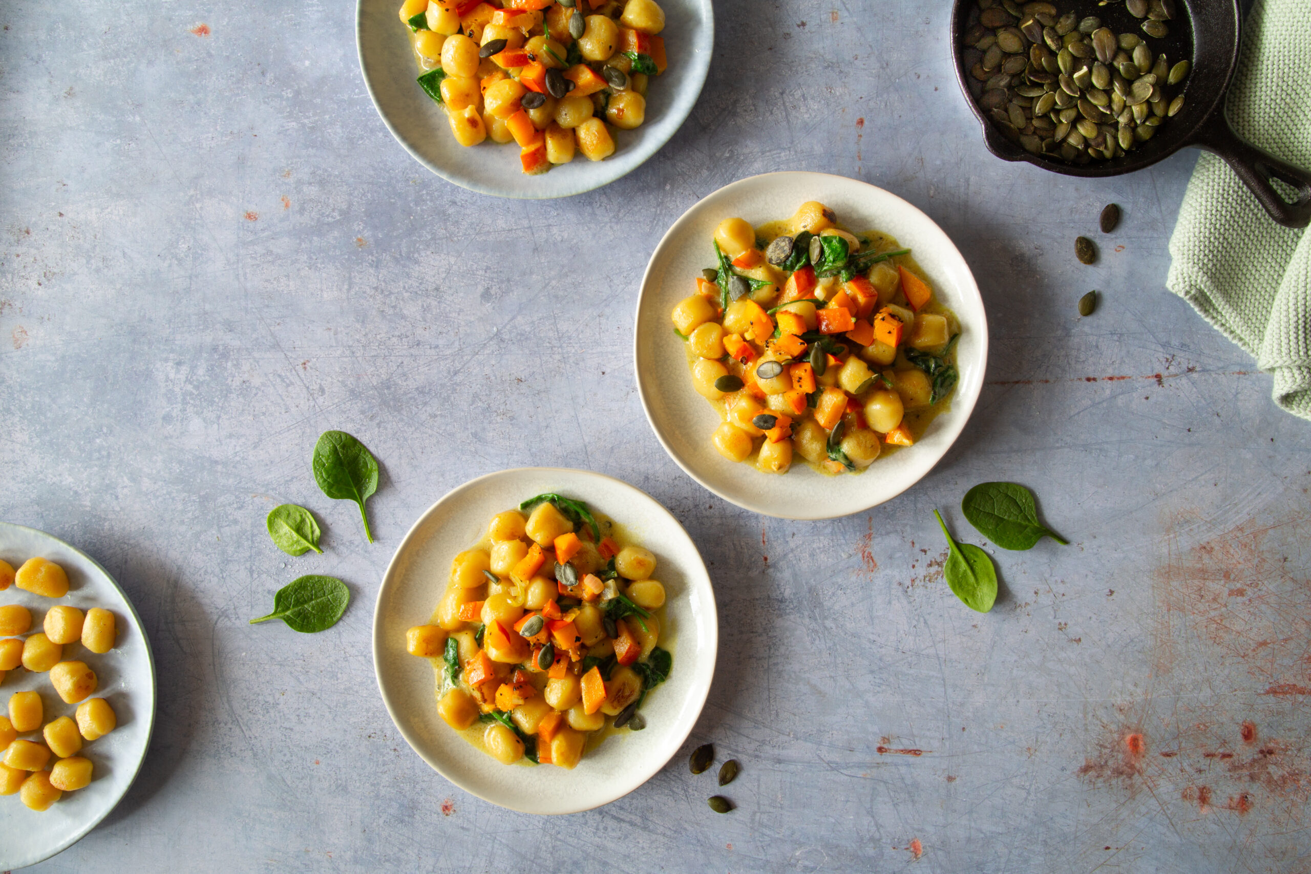 Hokkaido Gnocchi mit gerösteten Kürbiskernen und Spinat. Die gelbliche Farbe der Kürbis Gnocchi sticht besonders toll hervor auf dem hellblauen Untergrund.