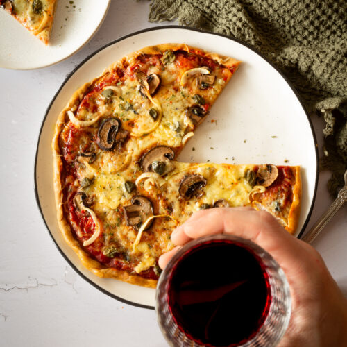 Runde Pizza mit Pilzen, Zwiebeln und Kapern. Dazu einem Glas Rotwein.