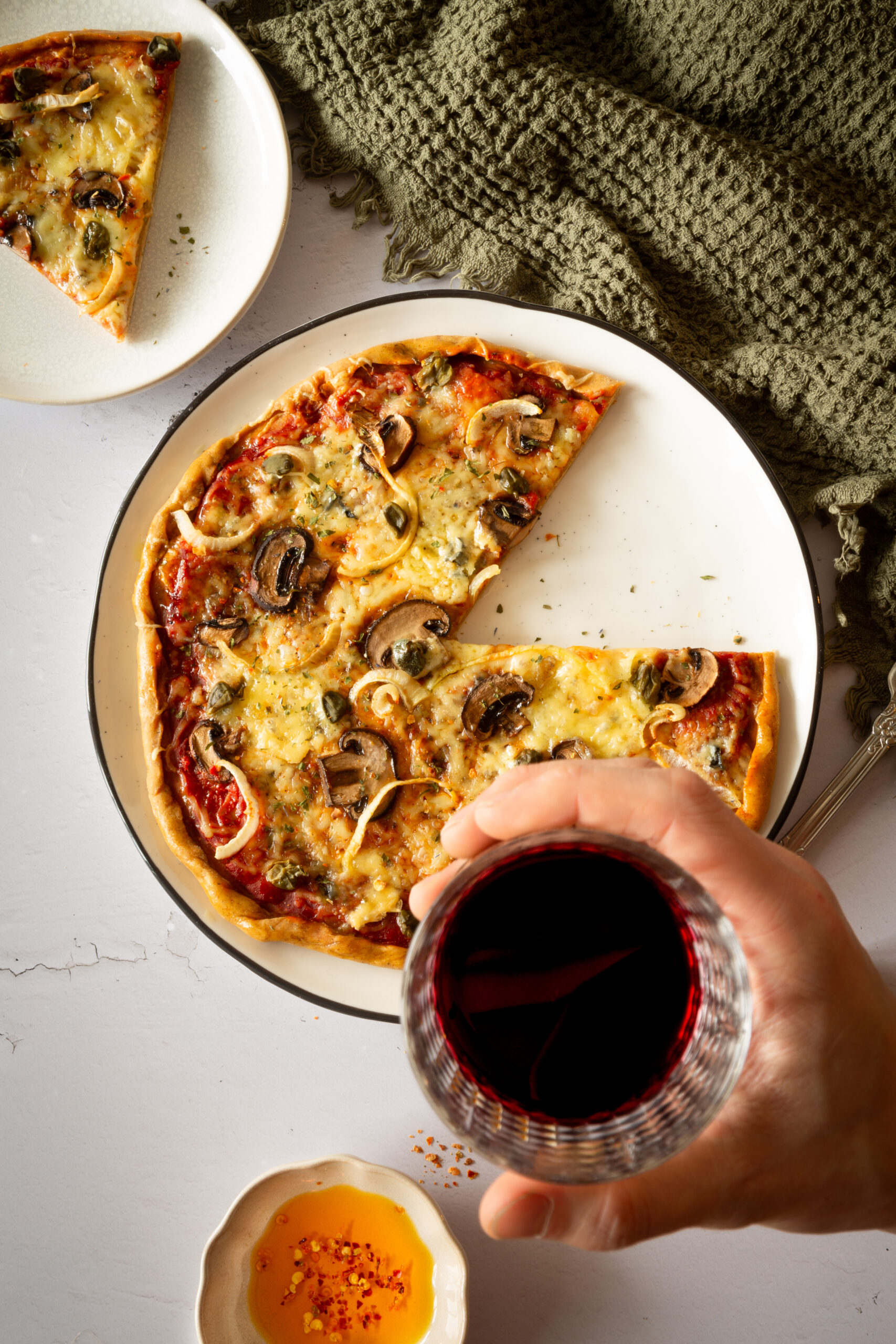 Runde Pizza mit Pilzen, Zwiebeln und Kapern. Dazu einem Glas Rotwein.