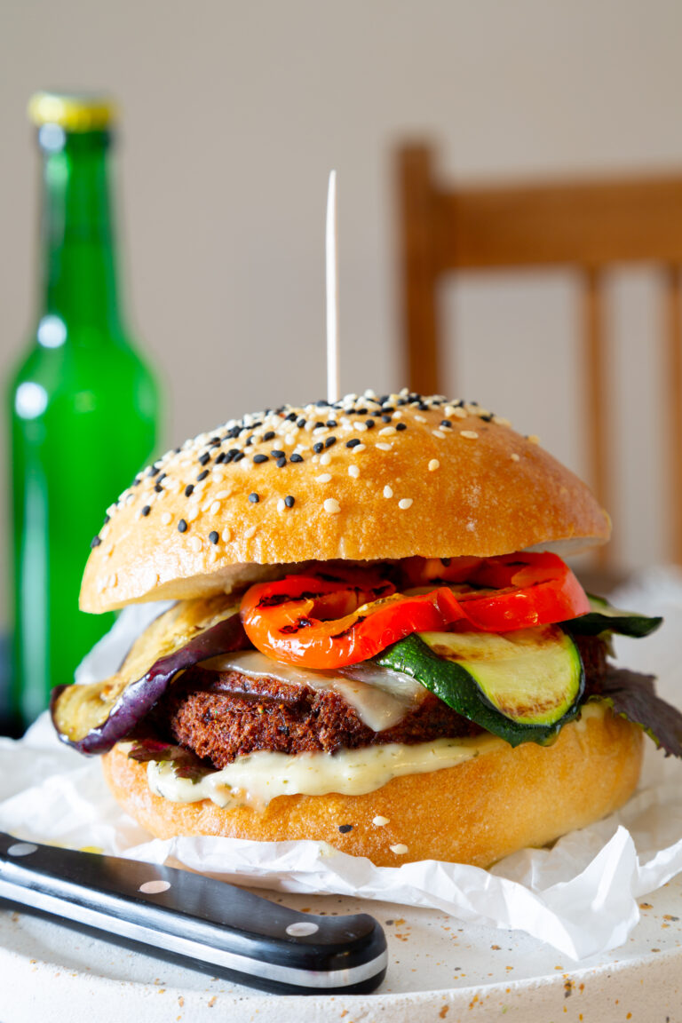 Saftiger Veggie Burger mit buntem Grillgemüse serviert mit einer kalten Flasche Bier.