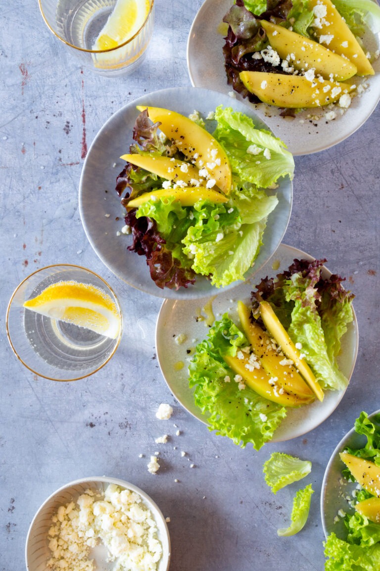 Knackiger Lollo Rosso & Lollo Bianco Salat mit strahlend gelben Mangostreifen, serviert mit Feta.
