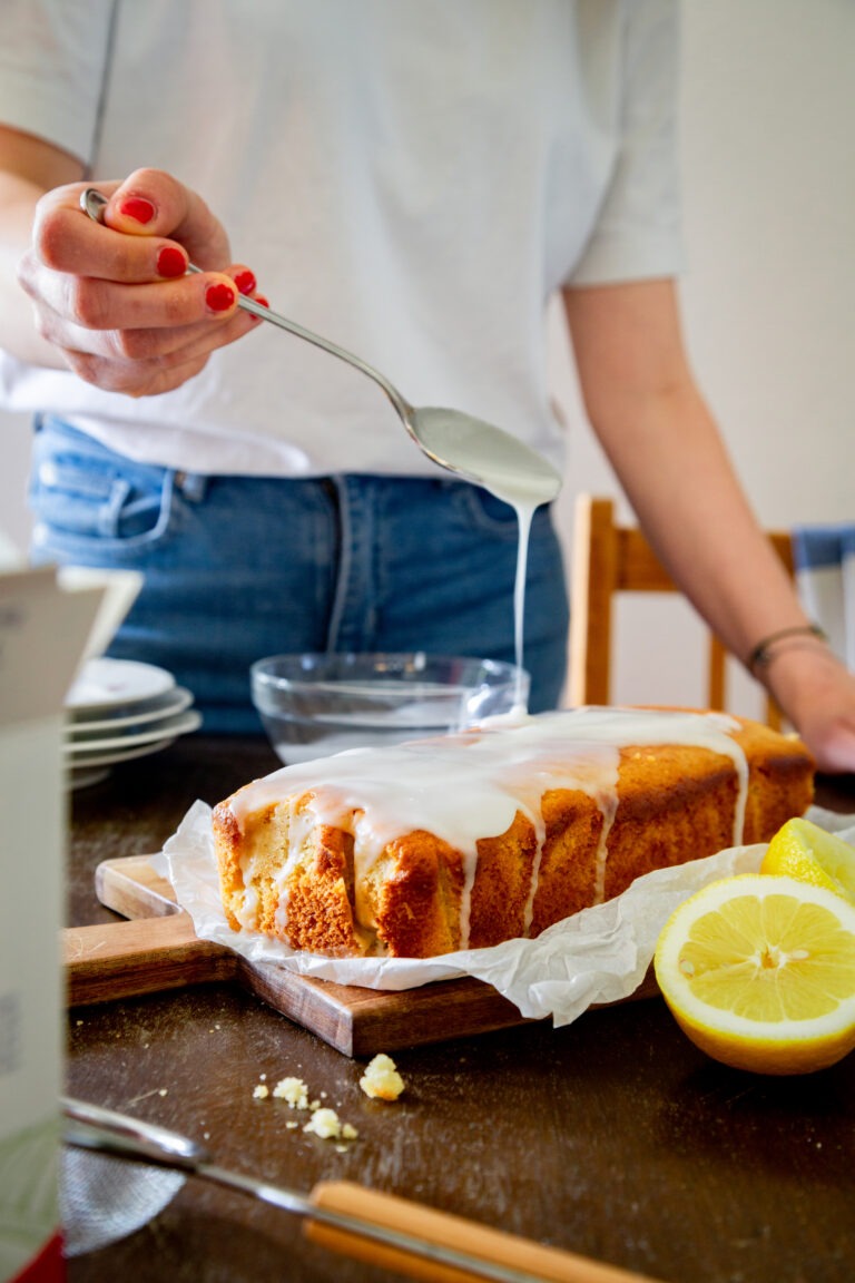 Ein Zitronen-Kuchen wird gerade mit Puderzucker-Glasur überzogen.