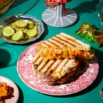 Grilled Cheese Sandwich mit Kimchi, fotografiert im Retro Stil vor rotem Vorhang und grünem Untergrund.